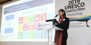 Jyoti Hosagrahar standing at a podium in front of a slide presentation.