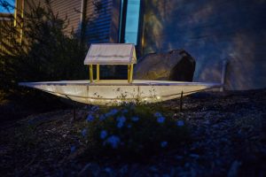 One paper boat lit up and placed in a garden at night time.