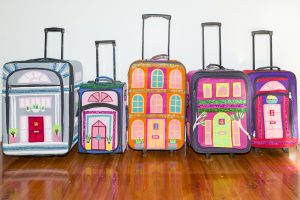 Five small suitcases with extendable handles decorated to look like tiny houses.