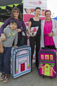 Four people posing and smiling with two small suitcases decorated to look like tiny houses.