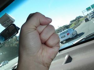 Image of a person waving their fist at traffic through the windshield.