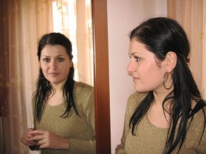 A woman is looking at her reflection in a mirror.