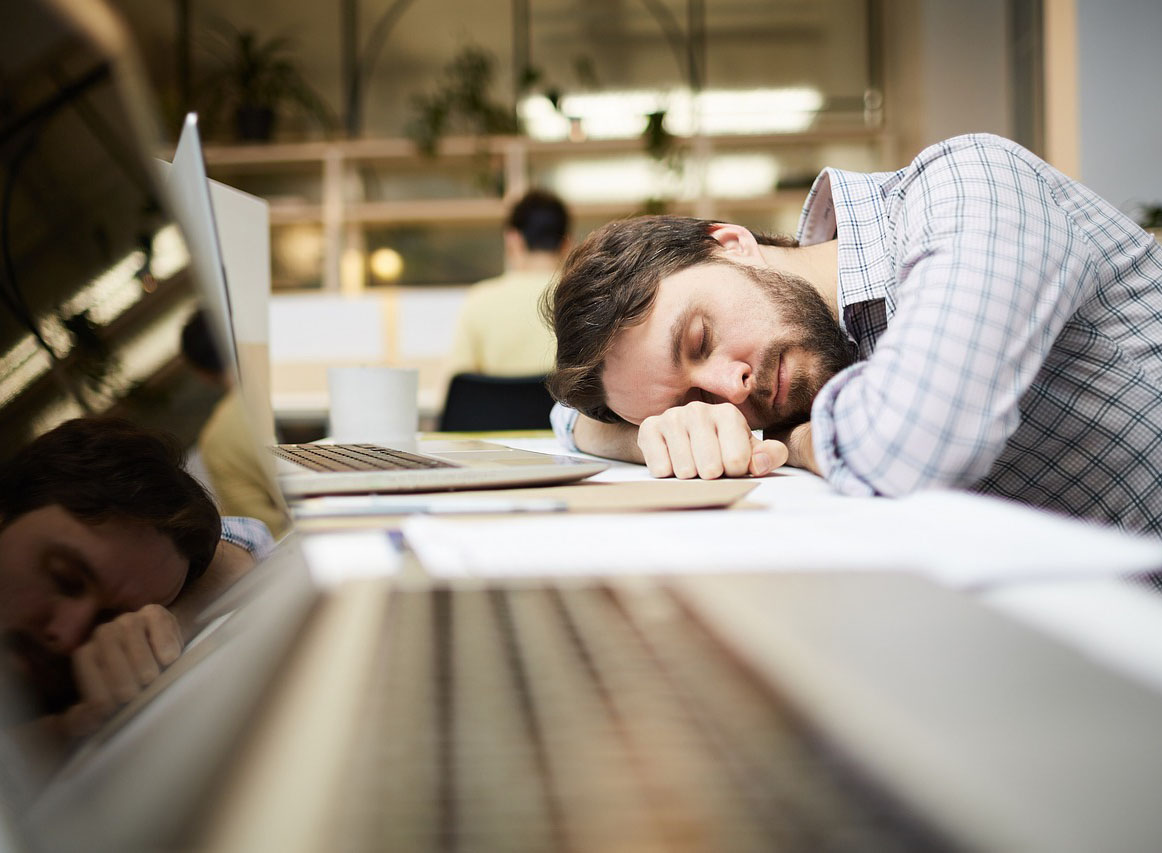 Man asleep behind a laptop.